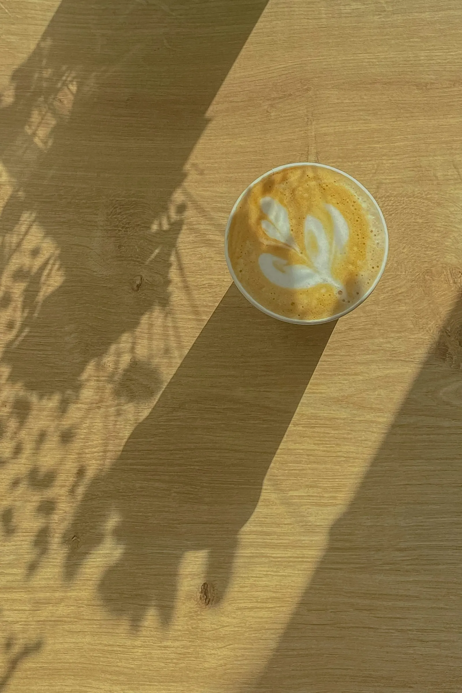 Café con arte latte sobre una mesa de madera con sombras